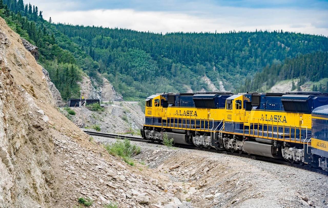 A railroad passenger train going into a mountain curve through a forest in Alaska, USA.